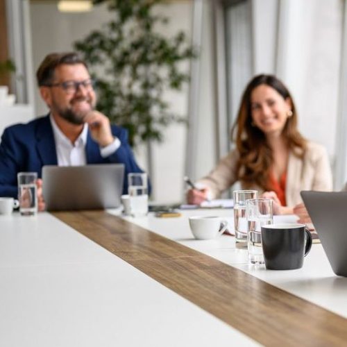 Happy businesswoman talking over mobile phone and using laptop while coworkers collaborating in board room